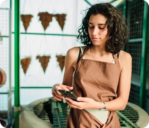 Mujer emprendedora sonriente en su floristería usando celular para recibir pagos con Poket