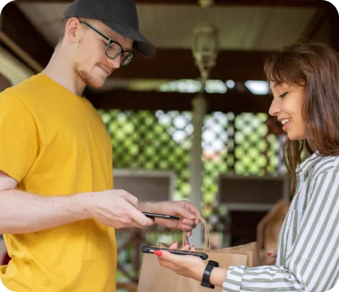 Hombre rapartidor sonriente usando celular para cobrar con Poket, entregando un delivery a mujer sonriente